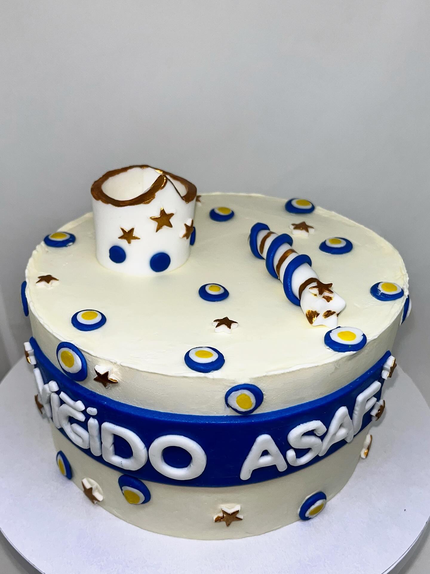 Gâteau blanc et bleu avec motifs ronds jaunes, étoiles dorées, décors modelés et prénom en relief