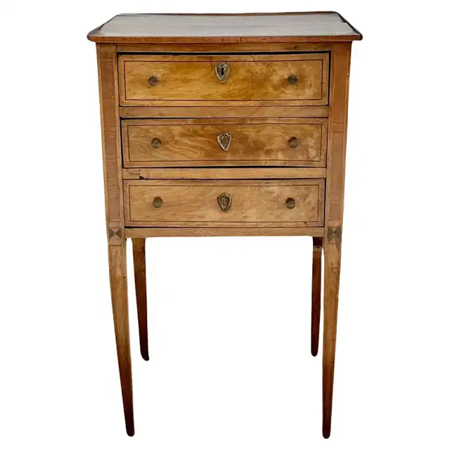 Honey-toned three-drawer stand with dark line inlay, shield-shaped escutcheons and slender tapered legs