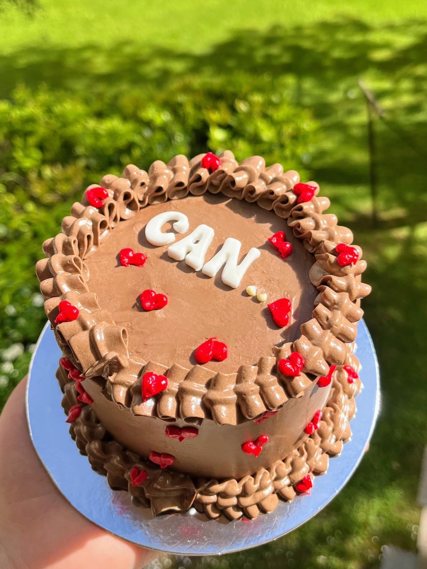 Gâteau couleur chocolat, orné de petits cœurs rouges et du prénom Can