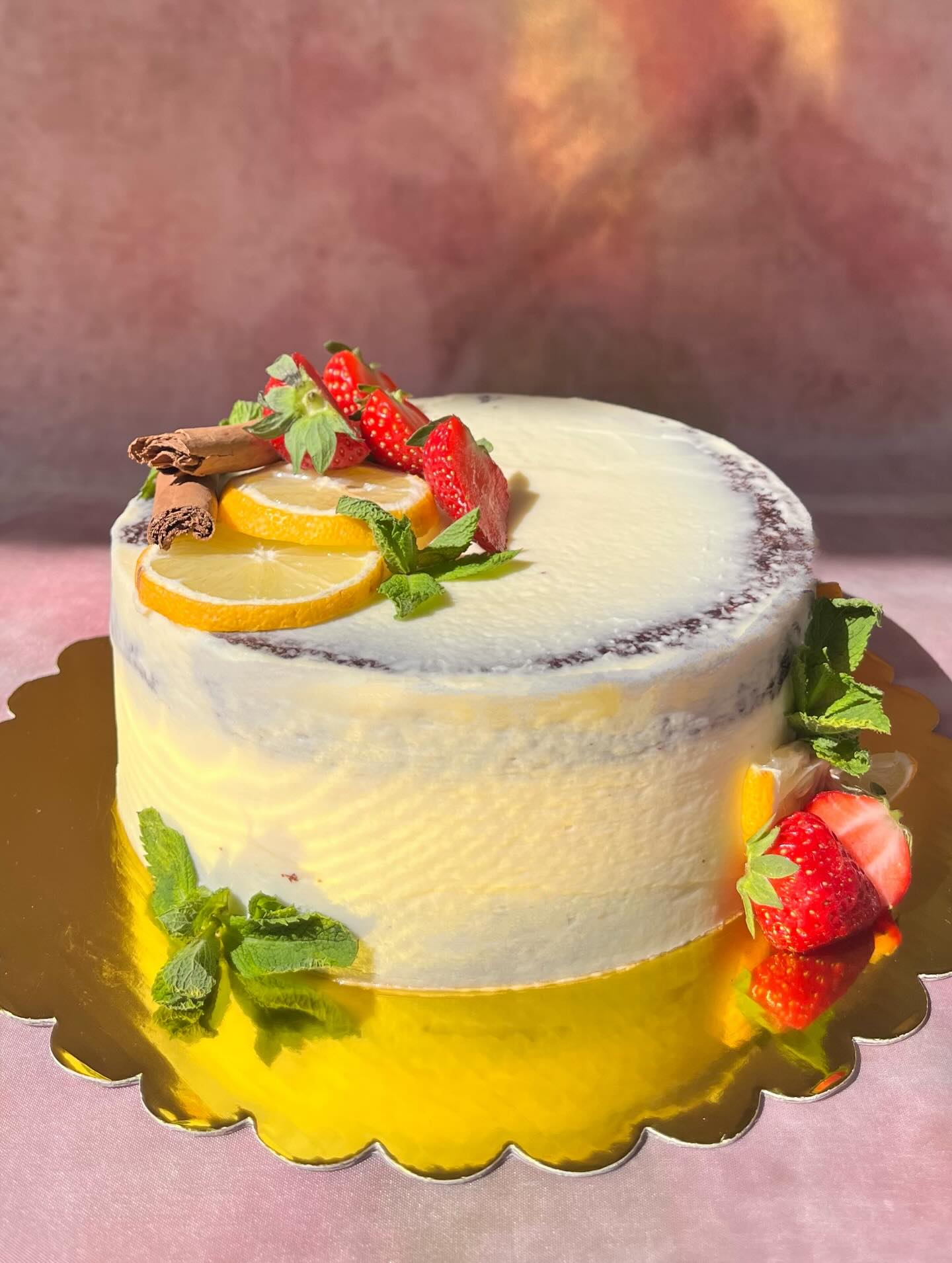 Gâteau au glaçage clair laissant apparaître les couches, décoré de fraises, rondelles de citron, menthe et bâtons de cannelle