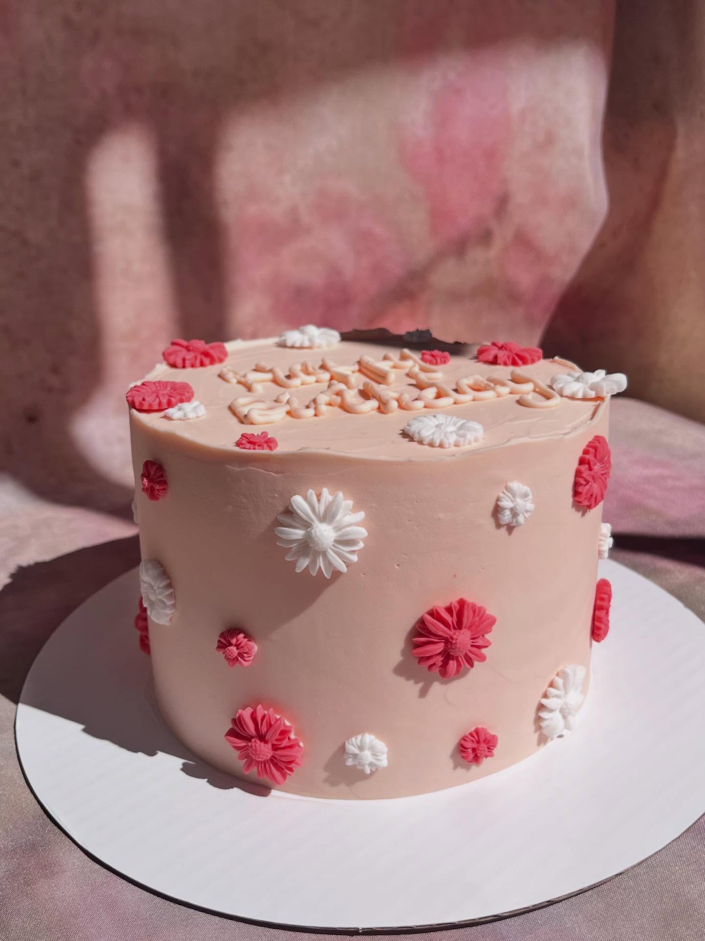Gâteau rose pâle parsemé de marguerites roses et blanches avec une inscription d’anniversaire
